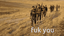 a group of soldiers walking down a dirt road with the words " fuk you " written on the bottom