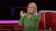 a woman in a green dress applauds while sitting on a nbc chair