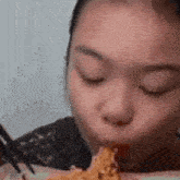 a young girl is eating a piece of chicken with chopsticks .