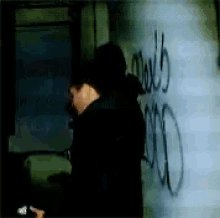 a man in a hooded jacket is spray painting graffiti on a wall that says mark 5