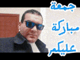 a man wearing sunglasses and a black jacket stands in front of arabic writing