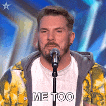 a man with a beard is singing into a microphone and the words me too are on the screen behind him