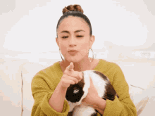 a woman in a yellow sweater holds a black and white cat and points at it