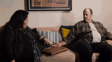 a man and a woman are sitting on a couch in front of a poster that says calamite