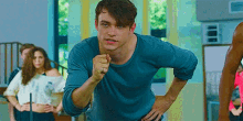a man in a blue shirt is pointing at the camera while standing in a room .