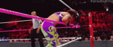 a woman in a purple and green outfit is wrestling in a ring .