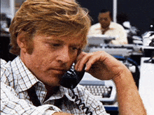 a man wearing a plaid shirt is talking on a telephone