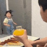 a man is holding a bottle of orange juice in front of a little girl