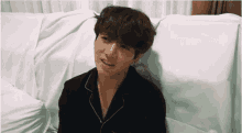 a young man is laying on a bed with white sheets and looking at the camera .