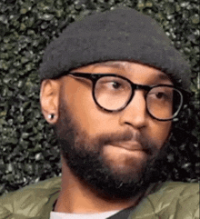 a man with a beard and glasses is wearing a beanie and jacket .
