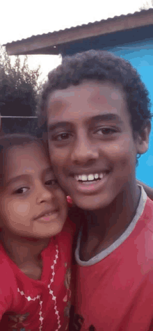 a boy and a girl are posing for a picture and the girl is wearing a red shirt .