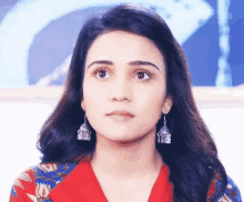 a woman wearing earrings and a red top looks at the camera