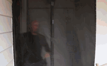 a man in a black shirt is standing in a dark room behind a screen door