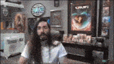 a man with long hair and a beard is sitting in a chair in a room with a sign that says uplay