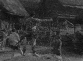 a black and white photo of a man with a sword in a village