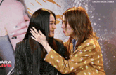 two women are touching each other 's faces in front of a sign that says dara live