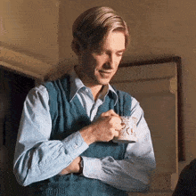 a man wearing a blue vest is holding a cup of coffee .