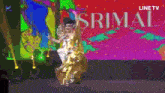 a woman in a gold dress is dancing on a stage in front of a line tv logo