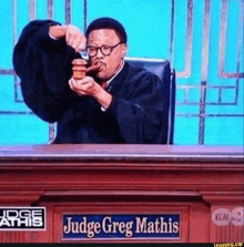 a man in a judge 's robe is sitting at a judge 's bench eating a hamburger .
