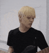 a man with blonde hair is playing a guitar in a black shirt .