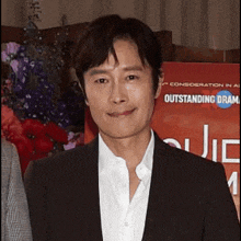 a man in a suit and white shirt is smiling in front of a sign that says outstanding drama .