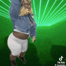 a woman in a denim jacket and white shorts is dancing in front of a green screen .