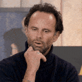 a man with a beard wearing a black turtleneck sweater and a ring on his finger