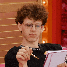 a man wearing glasses and a black shirt with the number 59 on it is writing in a notebook