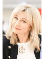 a woman wearing a black jacket and a white shirt has a necklace with a gold pendant