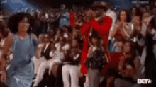 a man in a red jacket is singing into a microphone in front of a crowd of people .