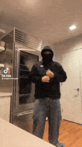 a man wearing a mask and a hoodie is standing in front of a refrigerator and a door with a tiktok watermark