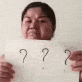 a woman is holding a sign with three question marks drawn on it .