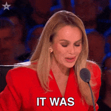 a woman in a red jacket speaking into a microphone with the words it was written on her face