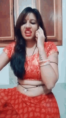a woman in a red saree is talking on a cell phone and making a funny face .
