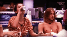 a woman drinking from a cup next to a shirtless man with the big brother brasil logo on the bottom