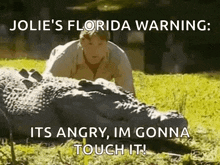 a man is laying on top of a large alligator in a field .