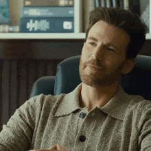 a man with a beard is sitting in a chair in front of a shelf with books on it