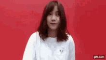 a woman in a white shirt is standing in front of a red background and making a funny face .