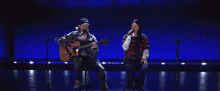 a man singing into a microphone while another man plays a guitar on a stage
