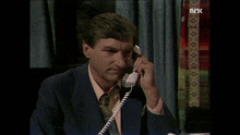 a man in a suit is talking on a phone with the letters nrk visible