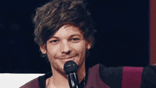 a young man is smiling while holding a microphone in front of him .