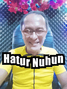 a man wearing glasses and a yellow shirt is smiling with the words hatur nuhun behind him