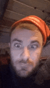 a man with a beard is wearing a red hat and making a face .