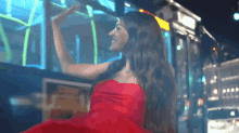 a woman in a red dress is smiling in front of a bus