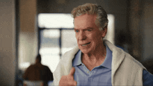 an older man wearing a blue shirt and a white vest giving a thumbs up