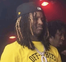 a man with dreadlocks wearing a yellow shirt and a black hat .