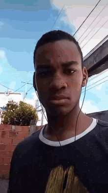 a young man wearing headphones looks at the camera while standing in front of a brick wall .