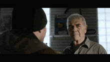a man in a black hat talks to an older man in a grey shirt