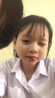 a little girl sticking her tongue out while wearing a white shirt