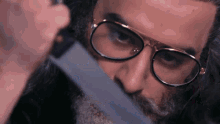 a man with glasses and a beard is holding a knife to his face